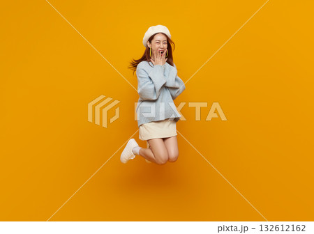 Jumping woman on yellow background, cheerful Asian girl in blue sweater and beret leaping midair copy space for fashion, lifestyle, youth, happiness, promotion, and social media banner. Jumping woman on yellow background, cheerful Asian girl in blue sweater and beret leaping midair copy space for fashion, lifestyle, youth, happiness, promotion, and social media banner. 132612162