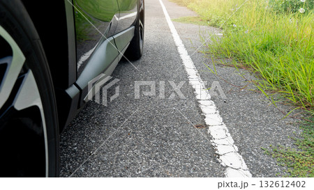 Car parking on the road with white line on the side of the road. Sides of the road are densely lush with green grass. 132612402