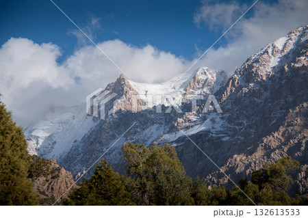 Snowcovered Mountains beneath Clear Blue Sky, framed by Lush Green Trees. Peaks and serene atmosphere make it an ideal scene for nature and landscape photography, suitable for prints and posters Snowcovered Mountains beneath Clear Blue Sky, framed by Lush Green Trees. Peaks and serene atmosphere make it an ideal scene for nature and landscape photography, suitable for prints and posters 132613533