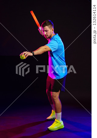 Man practicing sports skills with bat and ball in a colorful studio setting 132614114