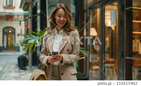 Dressed in a blazer, the woman walks down the street, glancing at her phone Dressed in a blazer, the woman walks down the street, glancing at her phone 132615902