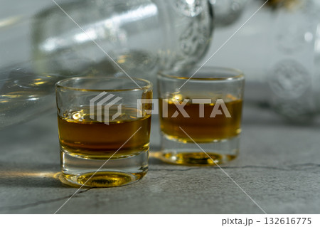 Two shot glasses of liquor are on a table next to a bottle Two shot glasses of liquor are on a table next to a bottle 132616775
