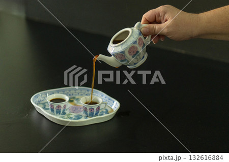 A person is pouring coffee into a teapot from a small cup A person is pouring coffee into a teapot from a small cup 132616884