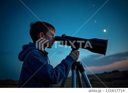 Close up face of curious kid child using telescope to explore moon surface. Little boy stargazing at night with a telescope to see galaxy from his room decorated bedroom with rocket in background. 132617714