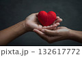 A pair of hands gently cradling a red heart representing love, compassion, care and kindness against a soft, neutral backdrop. 132617772