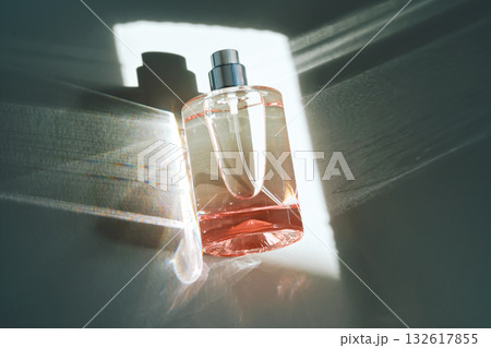 Pink perfume bottle on the light background in the rays of sun with highlights. 132617855