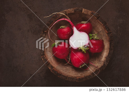 Fresh radishes displayed in a wooden bowl on a rustic surface for a wholesome culinary experience 132617886