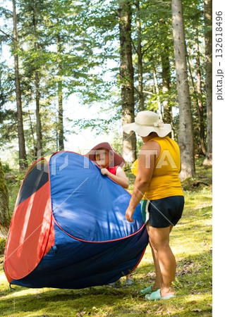 A child and adult set up a colorful pop-up tent in a forest. A sunny day of outdoor fun. 132618496