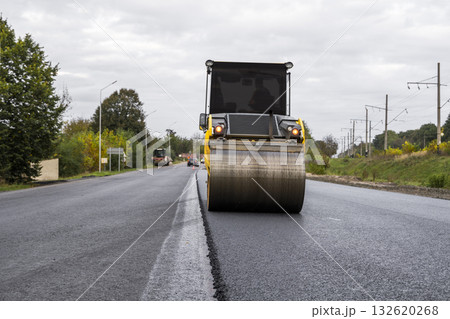 Yellow asphalt roller smoothing new road surface during roadworks on rural highway 132620268