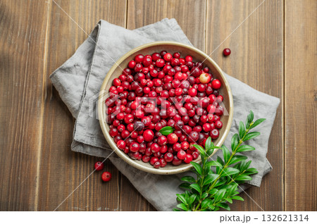 Fresh cranberries in a dark bowl on a wooden background with green branch and napkin. Fresh cranberries in a dark bowl on a wooden background with green branch and napkin. 132621314