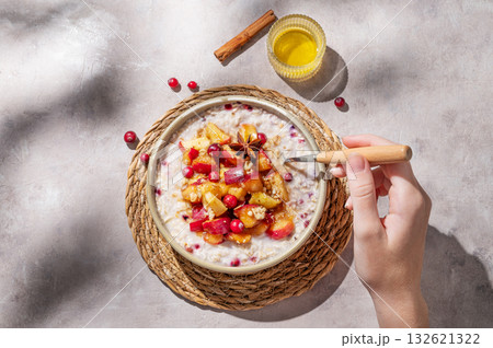 Hand holding spoon in to plate of oatmeal with apple, cranberry and cinnamon on a light background 132621322