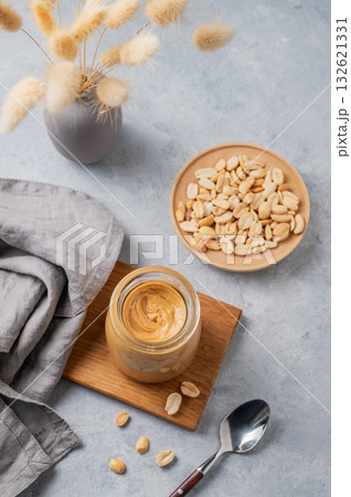 Creamy peanut butter in a jar on a wooden board on a light background 132621331