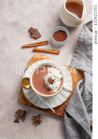 Hot chocolate in a cup with whipped cream and spices on a wooden board on a light background. Hot chocolate in a cup with whipped cream and spices on a wooden board on a light background. 132621351
