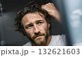 Close up of a thoughtful man with wet hair running his hand through it while looking in the bathroom mirror after taking a shower, showing signs of aging 132621603