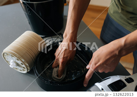 Skilled technician wiping interior components of air humidifier, vacuum cleaner positioned nearby for thorough dust removal and maintenance. Concept of maintenance modern home appliance. 132622013