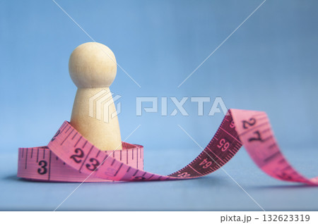 Wooden peg with stretched pink tape on blue background showing weight goal concept with customizable space for text or ideas. Wooden peg with stretched pink tape on blue background showing weight goal concept with customizable space for text or ideas. 132623319