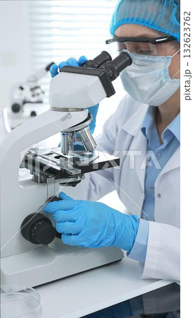 Female scientist analyzing sample through microscope, wearing protective lab gear during medical research investigation. Medicine, laboratory and science concept Female scientist analyzing sample through microscope, wearing protective lab gear during medical research investigation. Medicine, laboratory and science concept 132623762