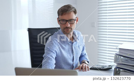 Male professional accountant calculating invoices and managing bills while reviewing financial reports in an office setting. Audit and taxes theme in business 132623770