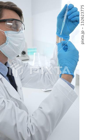 Scientist in a white lab coat, face mask, and gloves, analyzing a blue liquid in a test tube within a laboratory setting. Medicine, healthcare and science concept 132623775