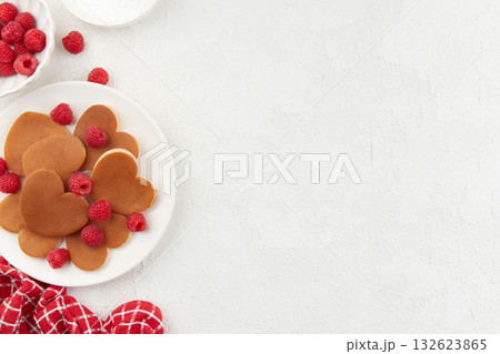 A heap of heart shaped pancakes on the white plate with raspberries on the white background 132623865