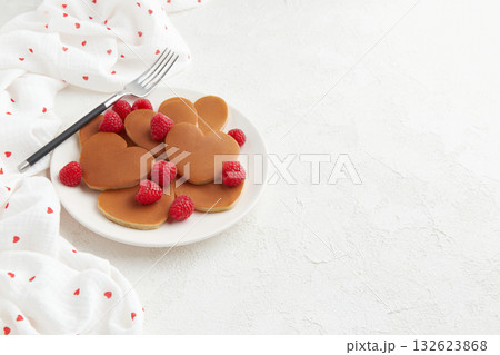 A heap of heart shaped pancakes with raspberries and a fork on the white plate on white background 132623868