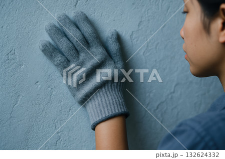 Person wearing gray wool glove touching textured blue wall with hand, highlighting sense of touch and tactile perception indoors, AI Generative 132624332
