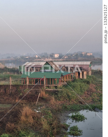 A wide shot of a large, modern building with a green roof, surrounded by lush vegetation and water, under a hazy sky A wide shot of a large, modern building with a green roof, surrounded by lush vegetation and water, under a hazy sky 132625127