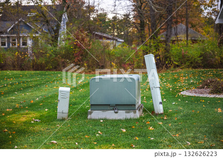 Utility boxes on a residential lawn surrounded by autumn foliage and houses in the background during fall season. 132626223
