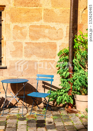 Empty blue metal chair and table on street near old stone house. vertical photo Empty blue metal chair and table on street near old stone house. vertical photo 132626465