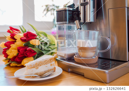 Cup of coffee with milk, piece of cake and tulips flowers on wooden kitchen table. Freshly brewed cappuccino espresso in coffee machine for breakfast. Stylish home interior decor. . High quality photo Cup of coffee with milk, piece of cake and tulips flowers on wooden kitchen table. Freshly brewed cappuccino espresso in coffee machine for breakfast. Stylish home interior decor. . High quality photo 132626641
