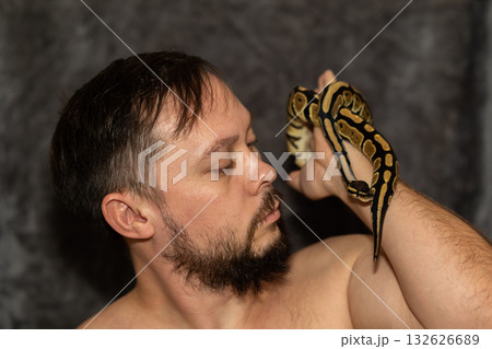 Portrait of caucasian man with Python regius snake on gray background. Selective focus. High quality photo Portrait of caucasian man with Python regius snake on gray background. Selective focus. High quality photo 132626689