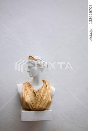 Antique head bust of woman against gray wall. Historical statue in golden dress himation. Ancient female face on light background. High quality photo Antique head bust of woman against gray wall. Historical statue in golden dress himation. Ancient female face on light background. High quality photo 132626702