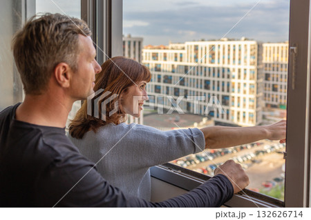 Man hugging his wife. Young couple moving in new apartmen. People looks out window at new houses. Concept new homes, new beginning. High quality photo 132626714