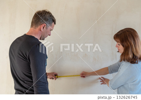 Young couple moving in new apartmen. People measure size of wall with tape measure. Concept new homes, new beginning. High quality photo 132626745