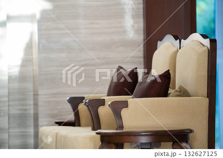 Sunlight shines on the elegant wooden sofa upholstered with ivory velvet fabric and a round coffee table set in a living room. Sunlight shines on the elegant wooden sofa upholstered with ivory velvet fabric and a round coffee table set in a living room. 132627125
