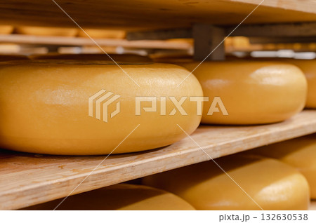 Cheese wheels made from cows milk aging on wooden shelves inside a cheese factory. 132630538