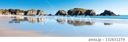 Breathtaking coastal panorama featuring a dramatic landscape of rugged rock formations pristine sandy beach and a serene ocean with stunning reflections under a clear blue sky 132631279
