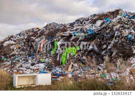 A massive mound of trash accumulates in the landfill, showcasing plastic, vegetation, and waste material against a cloudy backdrop 132633417