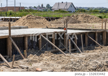 Construction crews lay a cement slab as part of foundation work for a new house in a developing neighborhood surrounded by fields 132633442