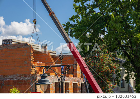 A crane is lifting building materials to an unfinished house in a residential area on a sunny day A crane is lifting building materials to an unfinished house in a residential area on a sunny day 132633452