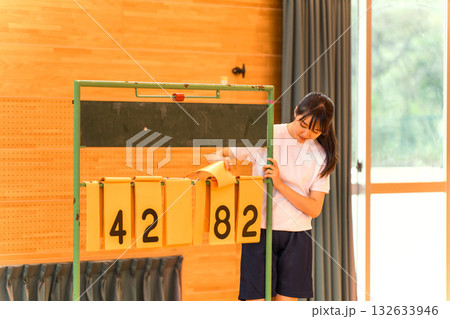 体育館でスコアボードをめくる体操着姿の女子生徒 132633946