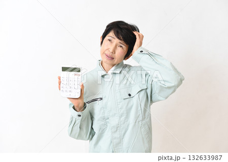 電卓を持ちながら困る作業服姿の中高年女性 電卓を持ちながら困る作業服姿の中高年女性 132633987