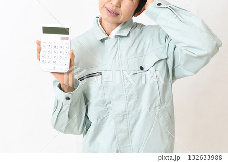電卓を持ちながら困る作業服姿の中高年女性 132633988