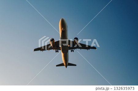 The image shows an airplane captured from a ground perspective, looking up towards the sky. The aircraft appears to be in mid-flight, with the landing gear extended, suggesting it is either about to 132635973