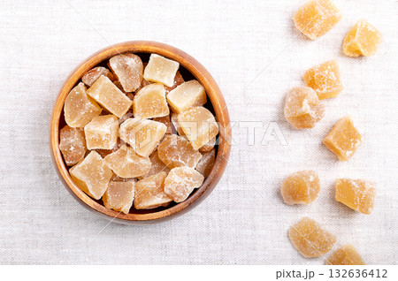 Candied ginger, crystallized ginger roots in a wooden bowl on linen. Rhizomes of Zingiber officinale, cut into block shaped chunks, boiled, and preserved with sugar. Sweet snack for the cold season. 132636412