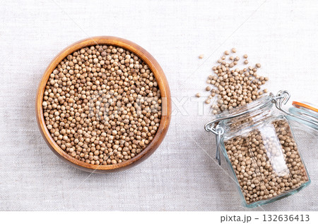 Whole and dried coriander seeds, in a wooden bowl on linen. Fruits of Coriandrum sativum, used as spice, with lemony citrus flavor, due to the terpenes linalool and pinene, that enhances when roasted. 132636413