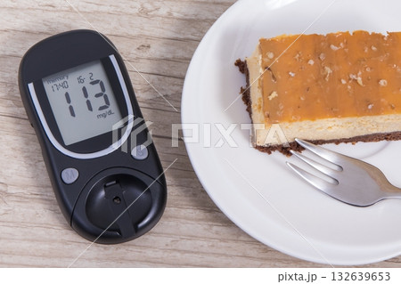 Glucose meter with high result sugar level and portion of sweet cheesecake Glucose meter with high result sugar level and portion of sweet cheesecake 132639653
