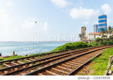 A coastal scene with rusted railway tracks beside the blue sea, lush greenery 132639936