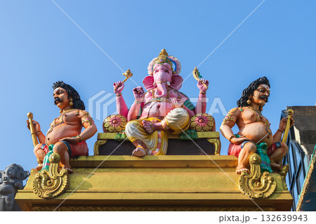 Vibrant scene featuring a pink Ganesha deity statue with two muscular guards Vibrant scene featuring a pink Ganesha deity statue with two muscular guards 132639943