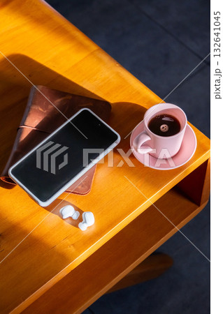 Coffee mug, smartphone, wireless earbuds and journal on wooden table. Coffee mug, smartphone, wireless earbuds and journal on wooden table. 132641045